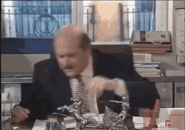 a man in a suit and tie is sitting at a desk with a statue on it .