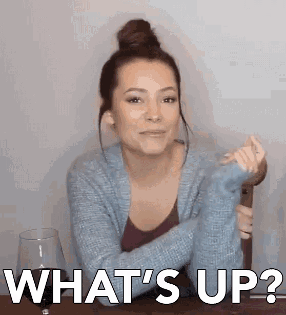 a woman is sitting at a table with a glass of wine and making a funny face and asking what 's up .