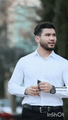 a man with a beard is wearing a white shirt and black pants and a watch
