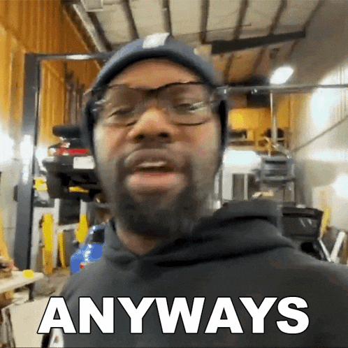 a man wearing glasses and a beanie says anyways in a garage