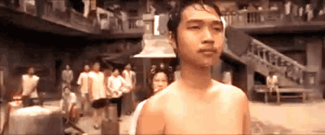 a shirtless man is standing in front of a crowd of people in a room .