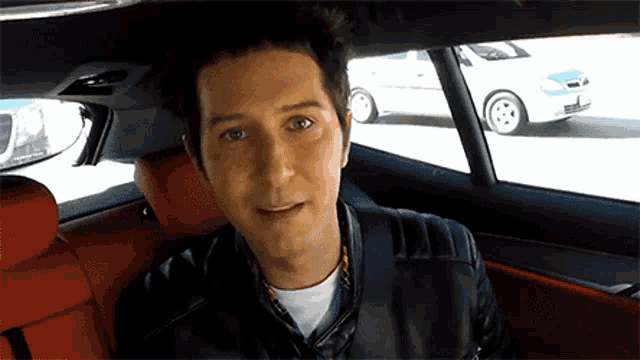 a man is sitting in the back seat of a car with a white car in the background