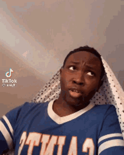 a man in a blue shirt is making a funny face while holding a sheet over his head .