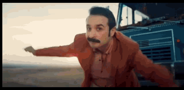 a man with a mustache in a red suit is running in front of a truck .