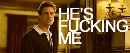 a man is standing in a room with the words `` he 's fucking me '' written on the wall behind him .