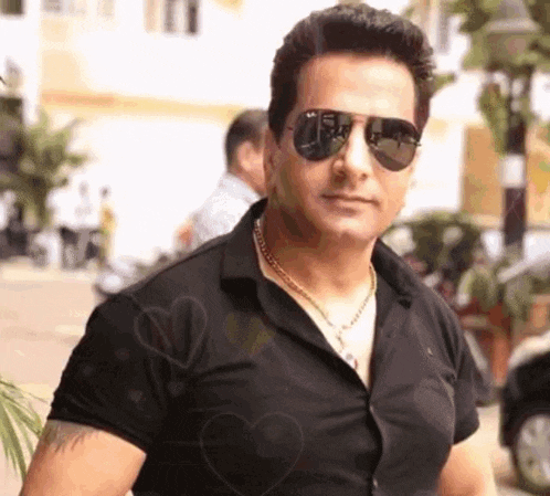 a man wearing sunglasses and a black shirt has a heart on his chest