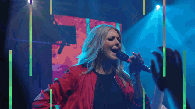 a woman in a red jacket singing into a microphone on a stage