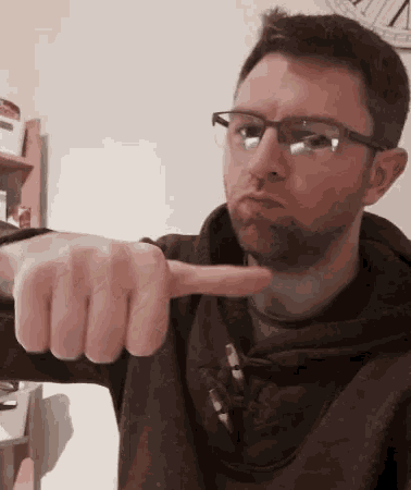 a man wearing glasses and a hoodie points at the camera
