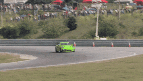 a green car is driving on a race track with a sign that says ' motorsport ' on it
