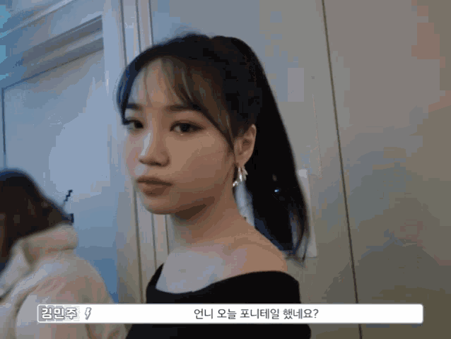 a woman wearing a black off the shoulder top is standing in front of a wall with korean writing on it