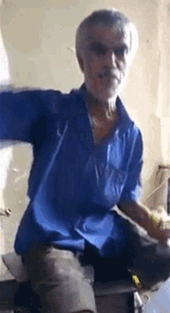 an older man in a blue shirt is sitting on a chair with his arms outstretched