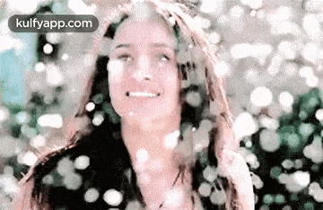a woman is smiling and looking at the camera while snow is falling from the sky .