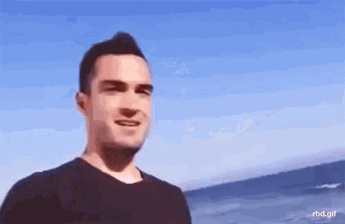 a man in a black shirt is standing on the beach looking at the ocean .