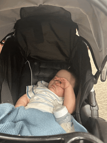 a baby is sleeping in a stroller with a bottle of avent on the floor