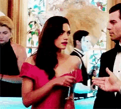 a woman in a red dress holds a glass of wine while talking to a man in a tuxedo