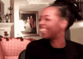 a woman is smiling in a living room with a picture of a man and woman in the background .