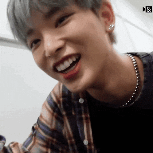 a young man wearing a plaid shirt and a necklace is smiling for the camera