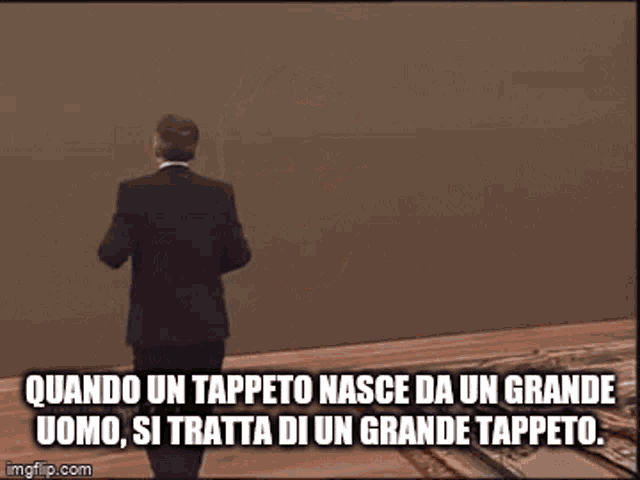 a man in a suit stands in front of a wall with a caption that says quando un tappeto