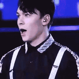 a young man wearing a black shirt and suspenders is making a surprised face .