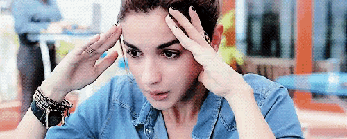 a woman is holding her head with her hands while wearing a denim shirt .
