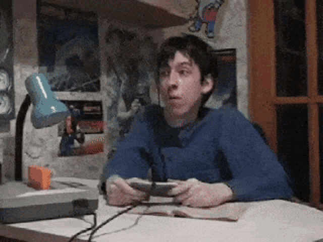 a man sitting at a desk playing a video game with a blue lamp behind him