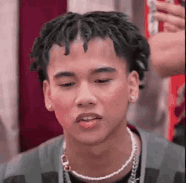 a young man with dreadlocks and a pearl necklace is looking down .