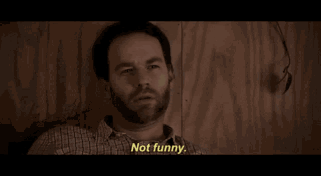 a man with a beard is sitting in front of a wooden wall and saying not funny
