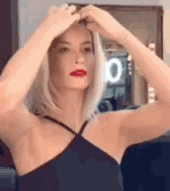 a woman is adjusting her hair in front of a mirror in a black dress .