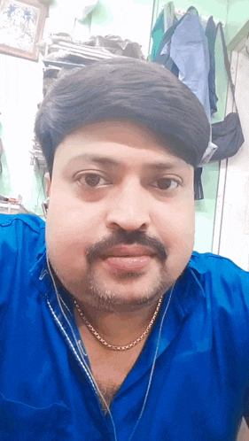 a man with a beard wearing a blue shirt and gold chain