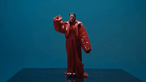 a woman in a long red coat is standing in front of a blue wall