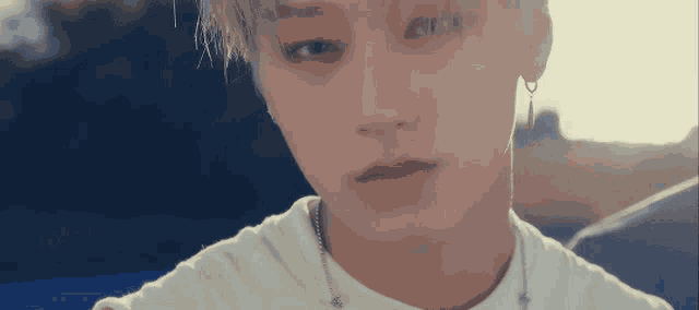 a close up of a young man 's face wearing a white t-shirt and earrings .