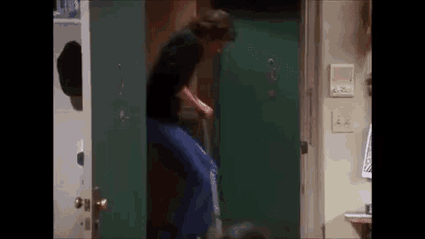 a man is standing in a doorway holding a blue bag and a broom .