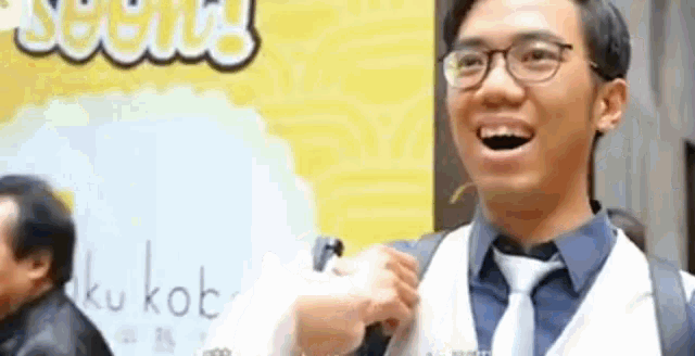 a man wearing glasses and a tie is smiling in front of a sign that says kukubob .