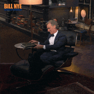 a man in a suit is sitting in a chair reading a book with bill nye written in the corner