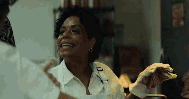 a woman wearing an apron and gloves smiles while talking to another woman