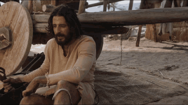 a man with a beard sits on the ground in front of a wheel