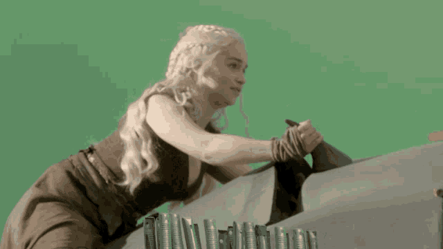 a woman with long blonde hair is sitting on a gray surface with a green background