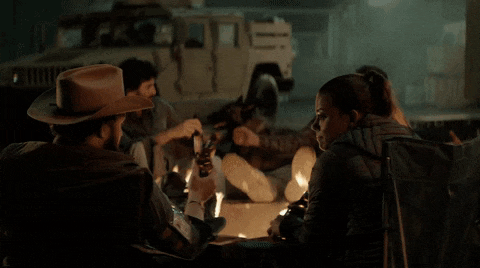 a group of people are sitting around a campfire drinking beer and eating food .