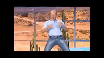a man in a blue shirt and jeans is dancing in front of a desert background .