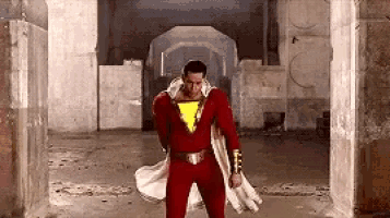 a man in a red superhero costume is standing in a hallway holding a cape .