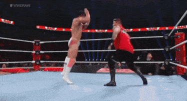 two men are wrestling in a wrestling ring and one of them is wearing a red shirt with the word raw on it .