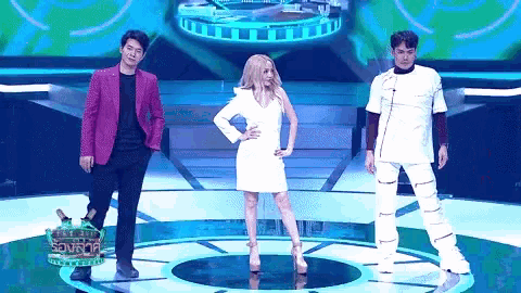 a woman in a white dress stands between two men on a stage in front of a sign that says source