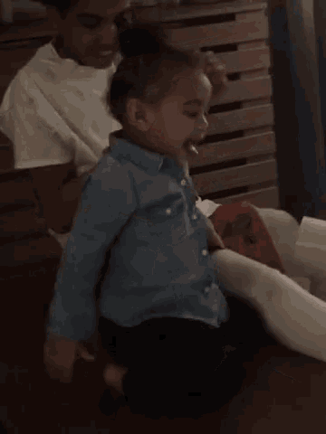 a little boy in a denim shirt is sitting on the floor with a woman .