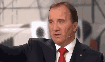 a man in a suit and red tie is talking into a microphone .