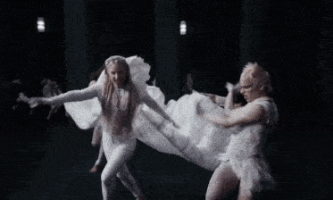 a woman in a white dress is surrounded by a group of dancers