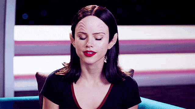 a woman wearing a black shirt and red lipstick is sitting on a blue couch with her eyes closed