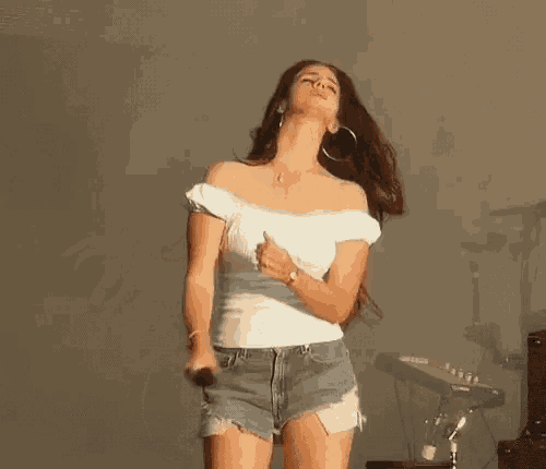 a woman is singing into a microphone while wearing shorts and a white top .