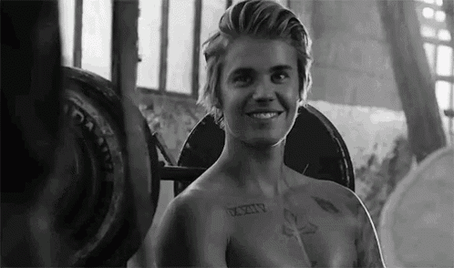 justin bieber is smiling while lifting a barbell in a gym .