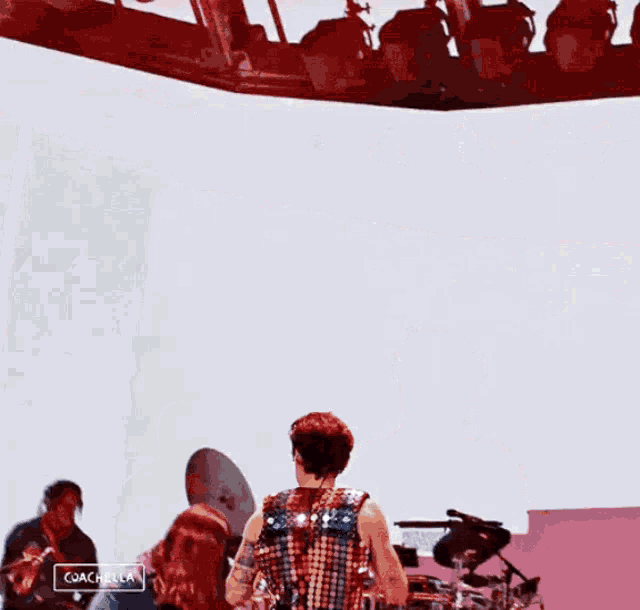 a man in a sequined vest is standing on a stage with a coachella logo in the corner
