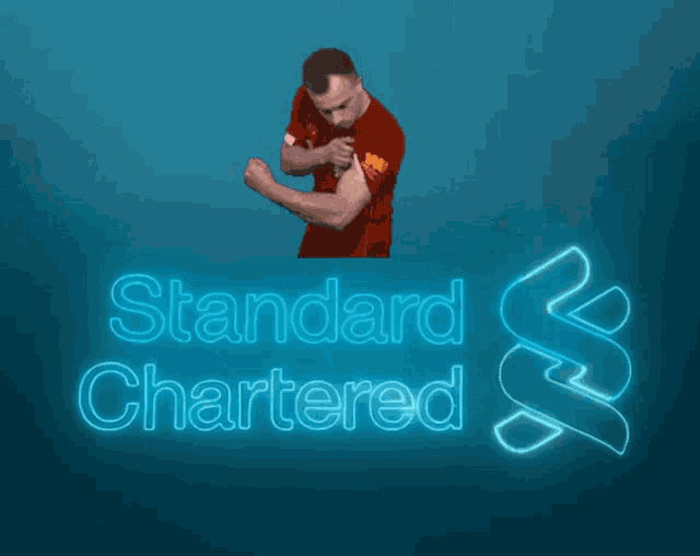 a man in a red shirt is flexing his muscles in front of a standard chartered logo